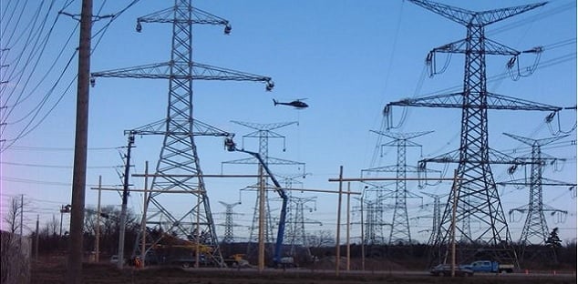 Image shows power lines and towers with cars driving below.