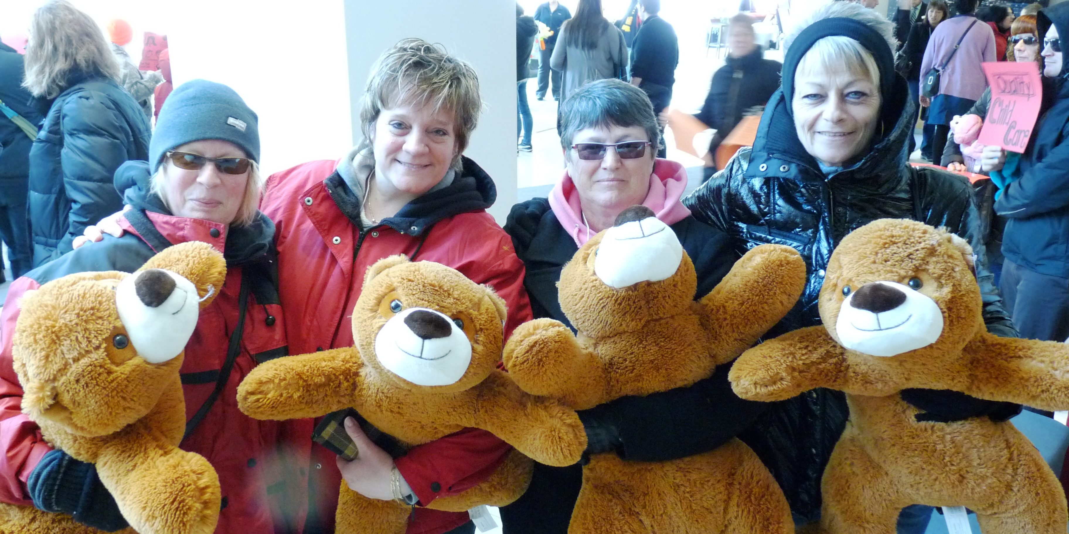 Image of 4 social services members looking at the camera and holding very large brown teddy bears