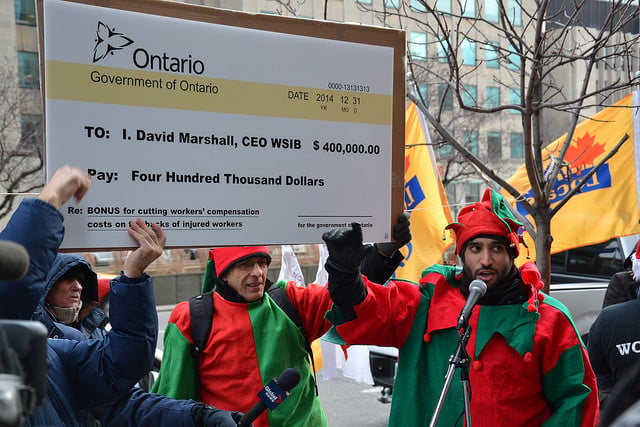 Two people dressed as christmas elves hold a cheque that reads 