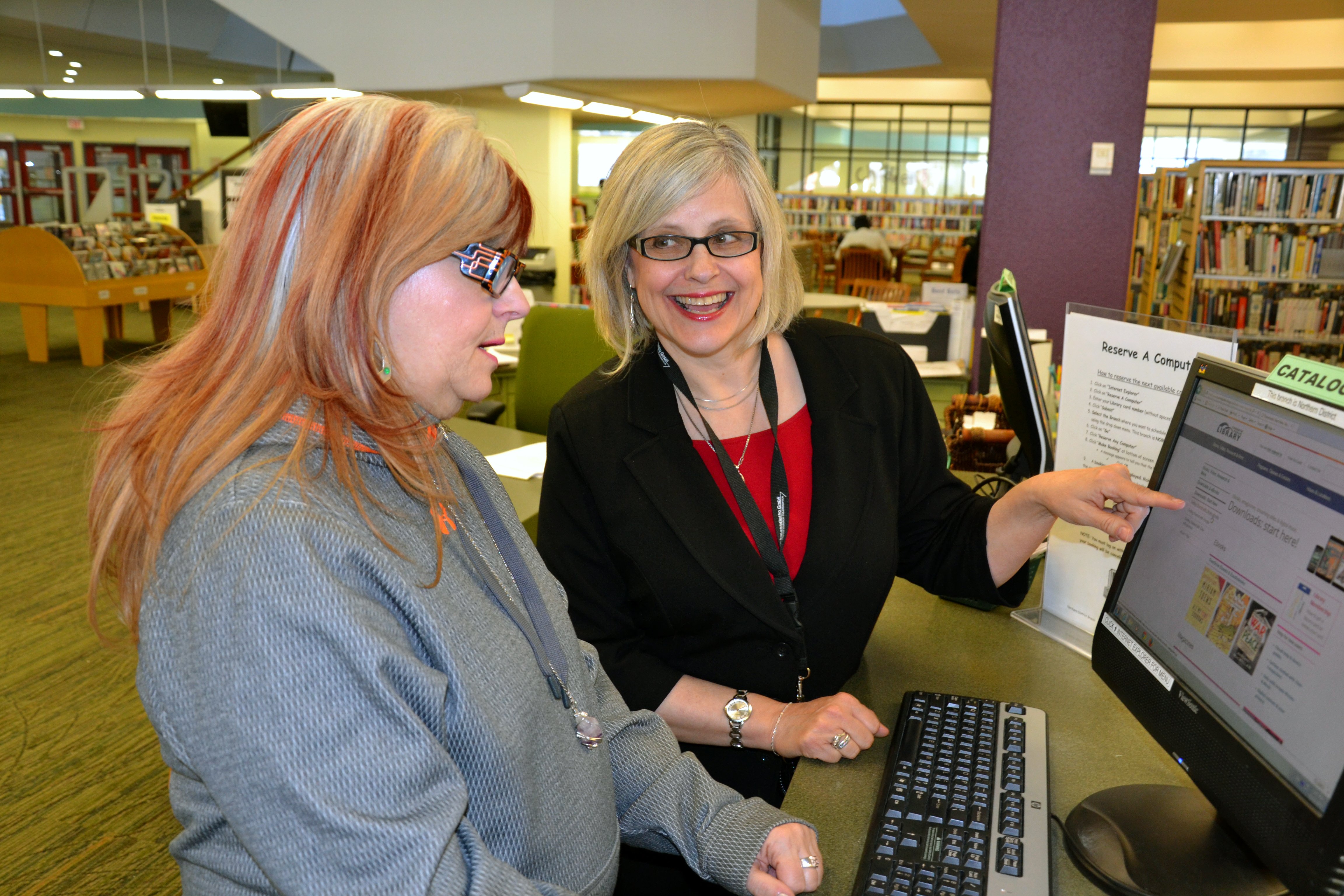 A library worker assists a library patron to use a computer
