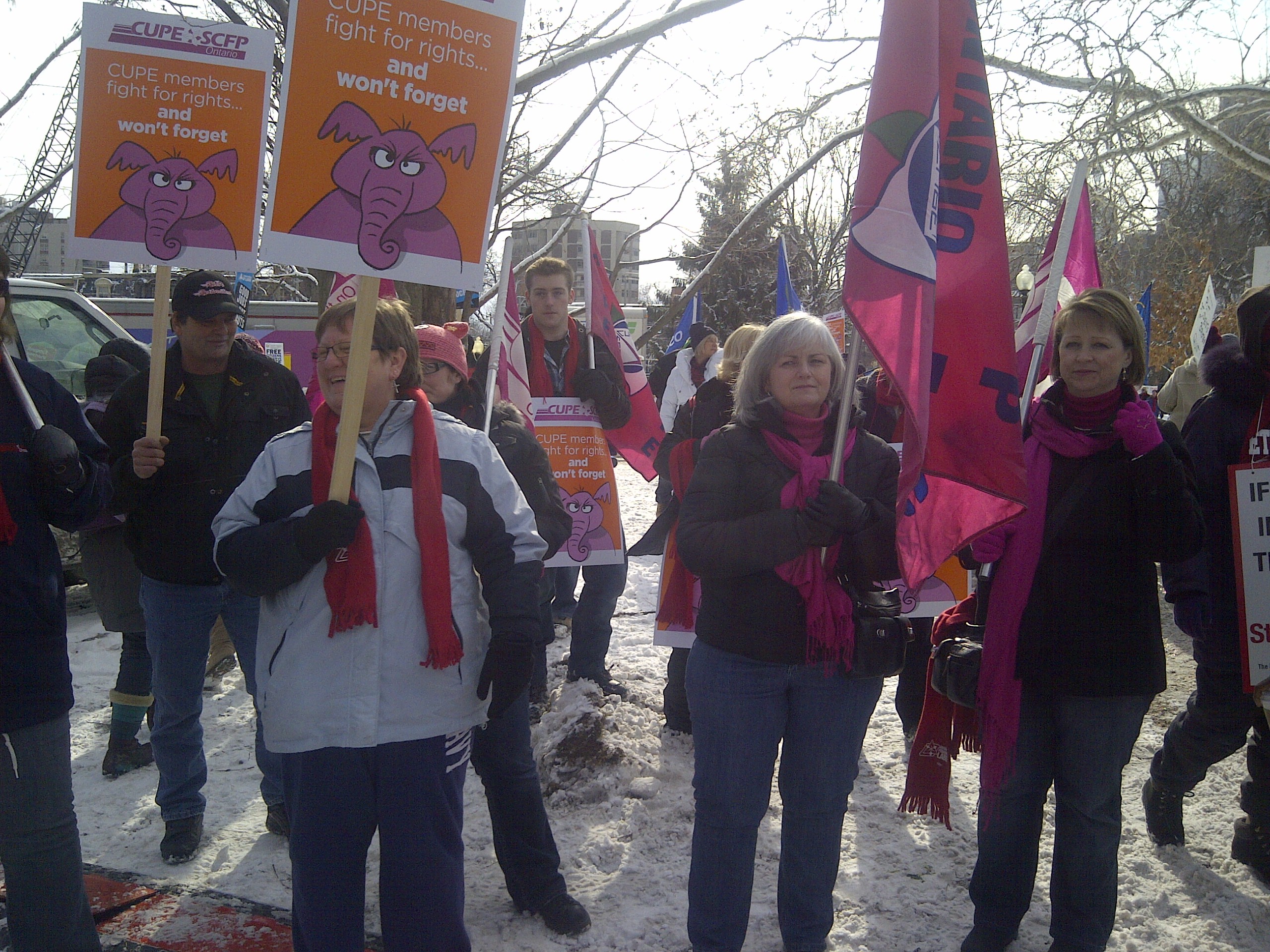 people stand outside with flags and signs. The signs read "CUPE members fight for rights... and won't forget" in Sault Ste. Marie and District