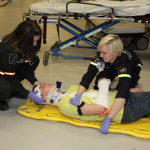 Two paramedics assistince a person lying on the floor with a neck brace