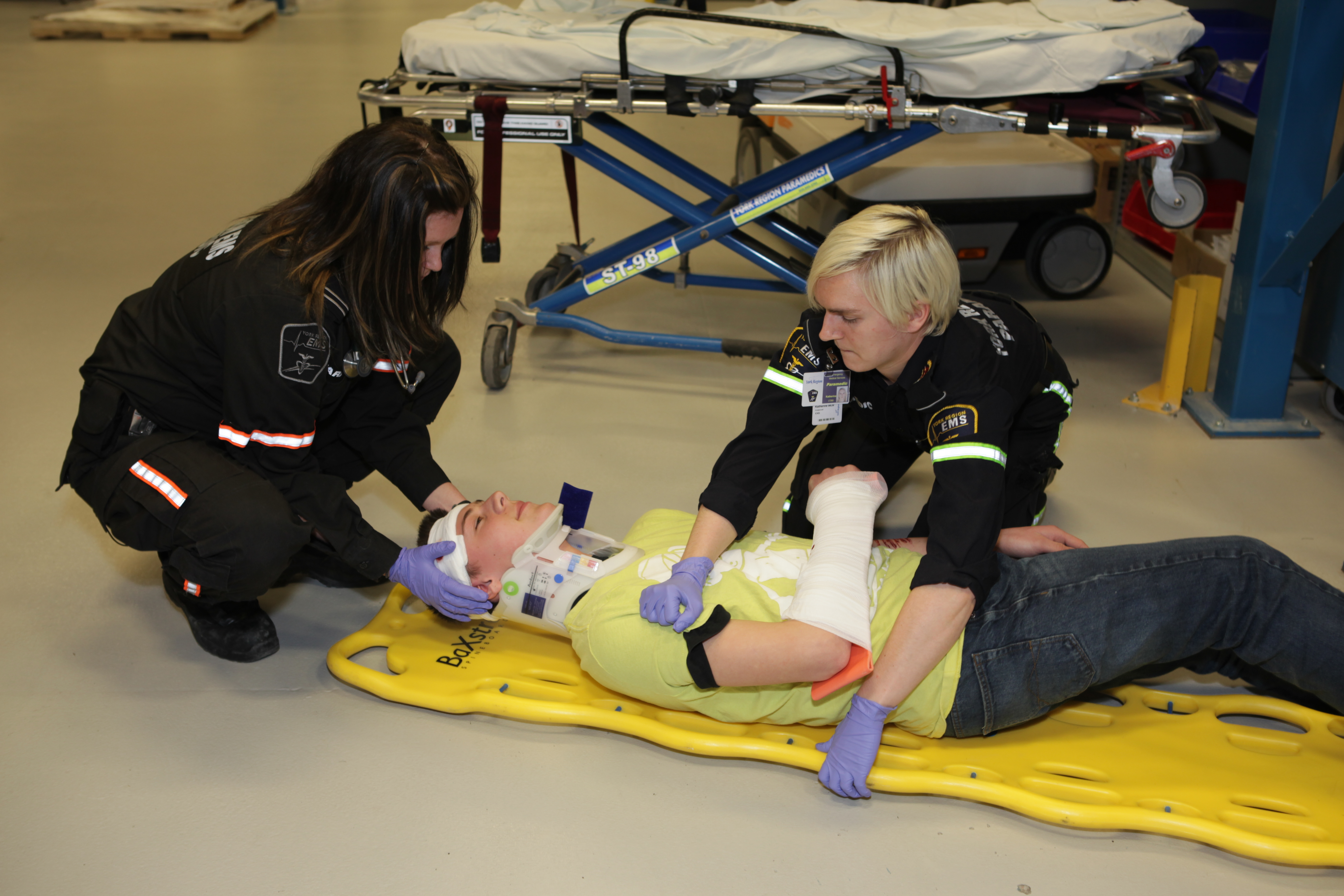 Two paramedics assistince a person lying on the floor with a neck brace