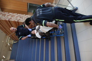 Two paramedics help a person in a wheelchair-like assistive device up stairs