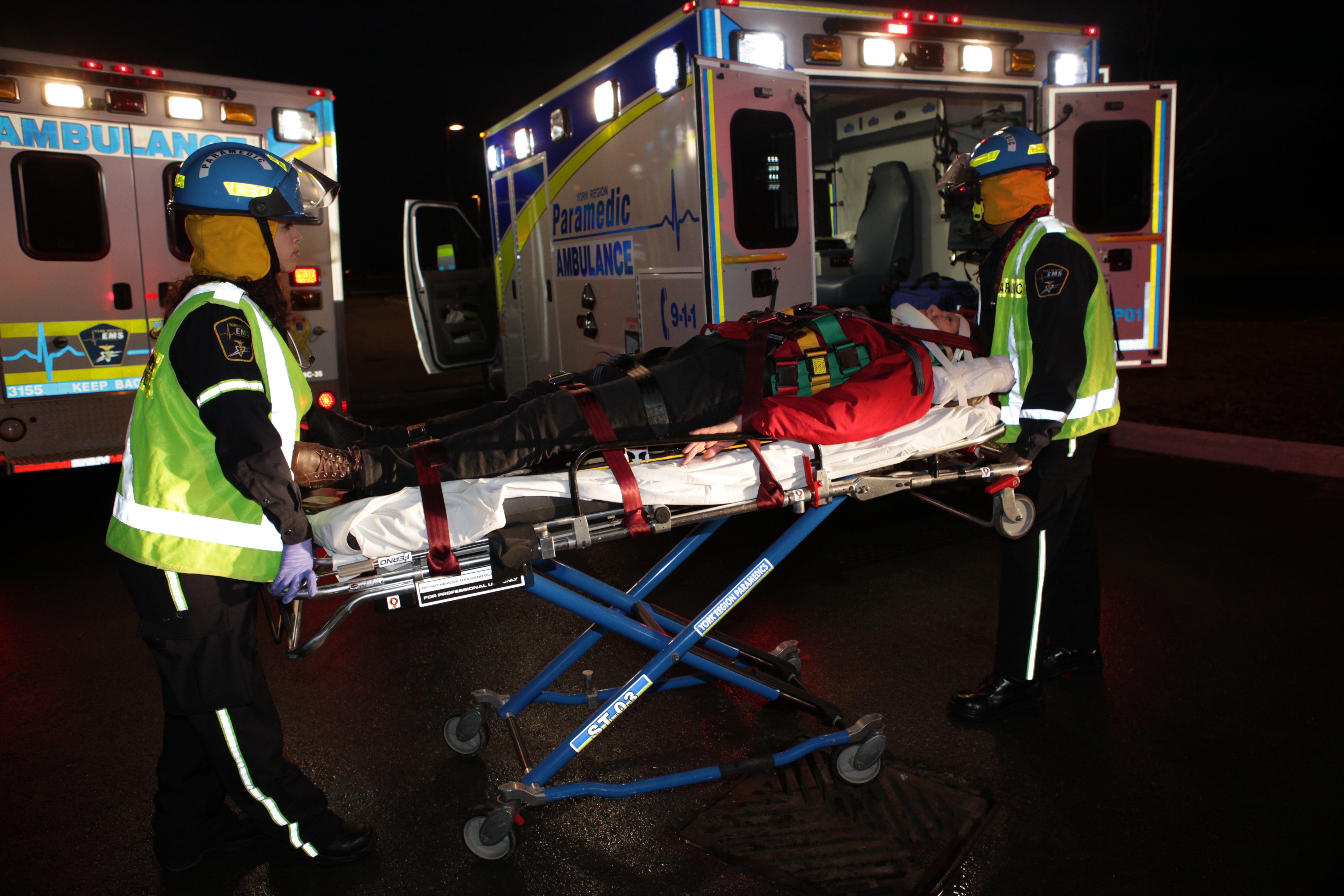 Two paramedics moving a person in a gurney at night in front of two ambulances