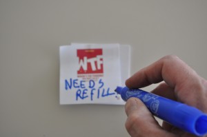 A person writing on a WTF sticker "Needs Refill"