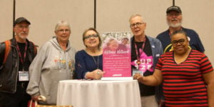 Image shows six Retirees' Network members gathered around a "Retirees" Network table display sign.