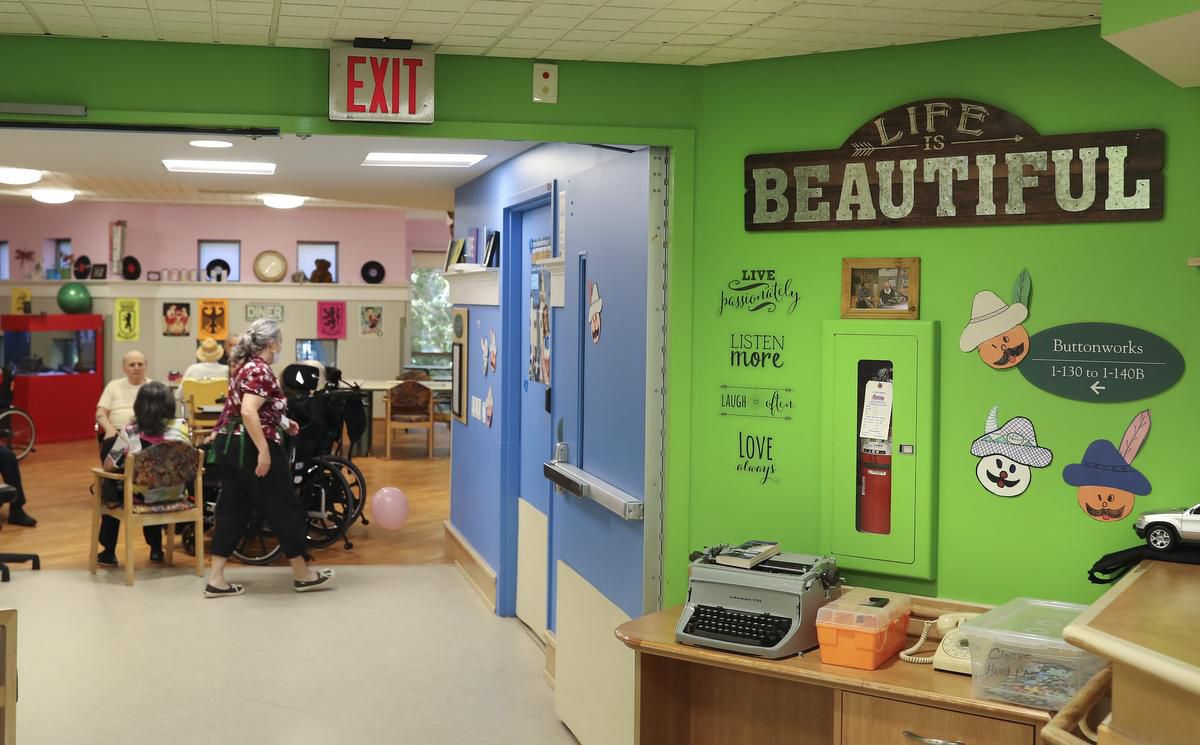 Image shows the inside of Sunnyside, a long-term care home, with bright green walls and a large wooden sign that says "Life is Beautiful." A few of the home's residents are in the photo's background.
