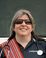 Image shows Leila Paugh, wearing a Metis sash across their shoulders, a stethoscope around their neck, sunglasses, and their paramedic uniform.