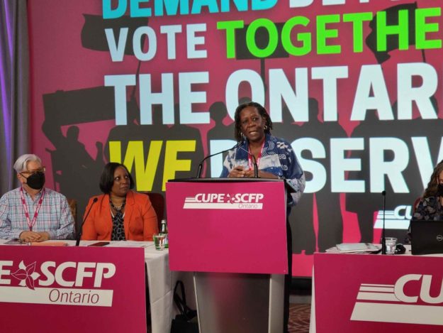Post-ConventionNewsletter_DrAkuaBenjamin_1May2022 Image shows Dr. Akua Benjamin at a podium with the CUPE Ontario Convention 2022 logo behind her. It reads "Demand better, vote together: the Ontario WE deserve." Fred and Yolanda are looking attentively at Dr. Benjamin as she speaks from a table directly to her right.