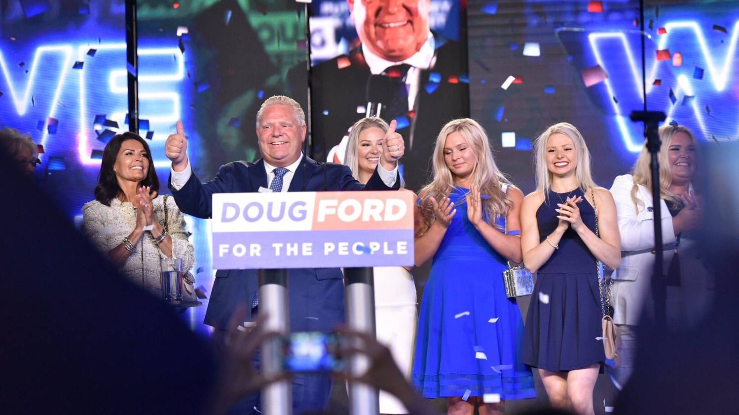 Ricochet-Fred-Angella-op-ed_9May2022 Image shows Doug Ford, with his family applauding behind him, at his own rally. He stands in front of a podium, giving the two-thumbs-up hand signal. The podium in front of him reads "Doug Ford: for the people."