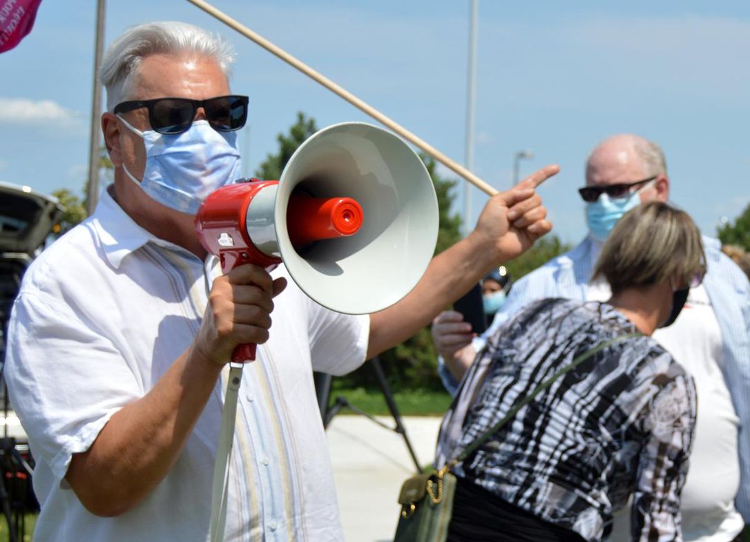 fred_hahn-op-ed_4May2022 Image shows Fred Hahn, outdoors, wearing a face mask, and speaking into a microphone as he points to the left with his left hand.